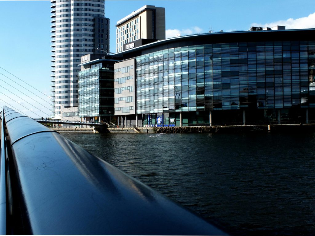 pexels-photo-396036-396036 Reflection of skyscrapers and waterfront architecture in Manchester, UK under clear blue skies.