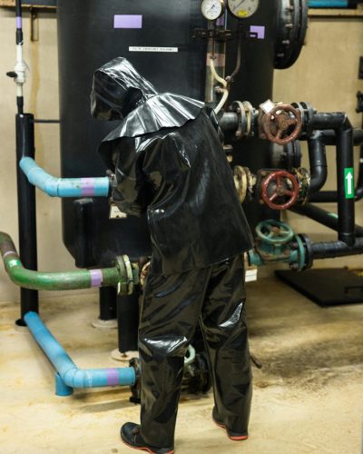 pexels-photo-16442681-16442681 Worker in black protective suit managing industrial equipment indoors.