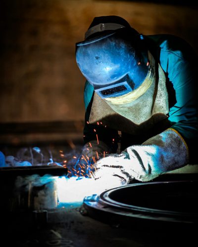 pexels-photo-27102112-27102112 Close-up of a welder working with sparks in a dimly lit workshop.